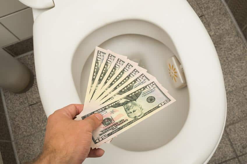 Hand throwing 100 dollar bills in toilet